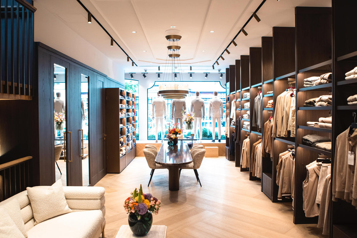 Interno dello store OGÉR di Amsterdam con armadi a muro in legno scuro, un lungo tavolo e maglieria